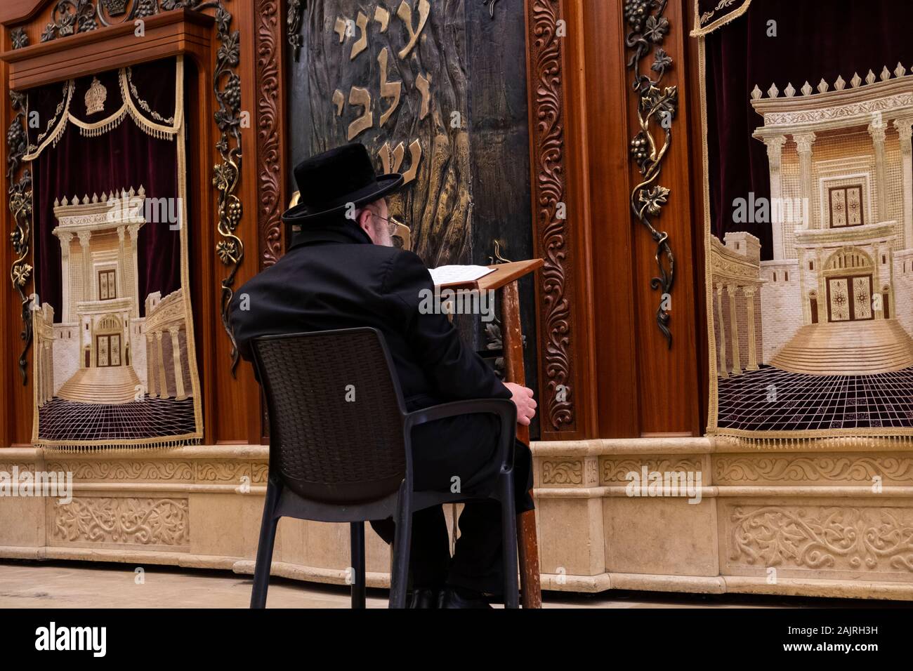 A Jewish worshiper praying at Torah Ark closet which contains the Jewish Torah scrolls decorated with a figure depicting the Biblical Jewish Temple Stock Photo