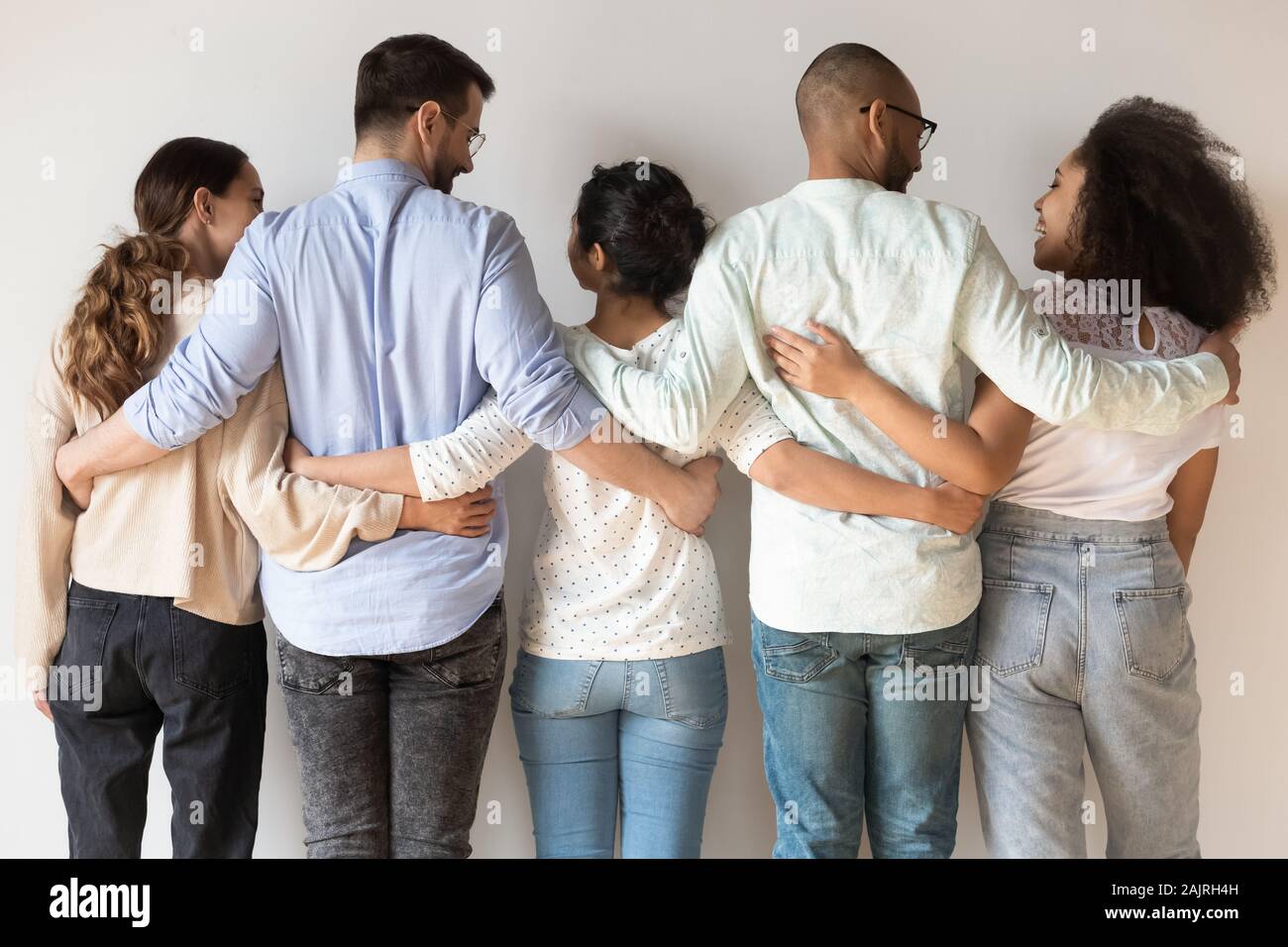 Back view of happy international young people stand hugging Stock Photo