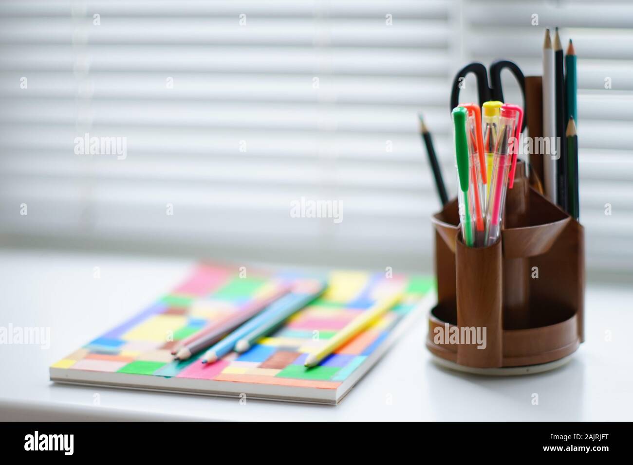 Stationery scissors and a set of colored pencils in a stand on a white table. Stock Photo