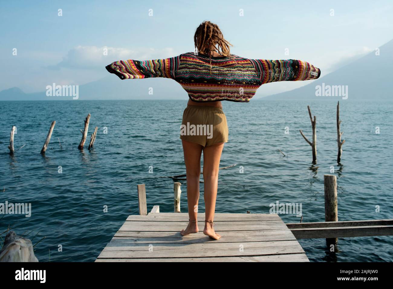 Rear view of attractive Caucasian woman dancing on a jetty. Outdoor lifestyle, solo travel, holiday, recreational concept. Lake Atitlán, Guatemala Stock Photo