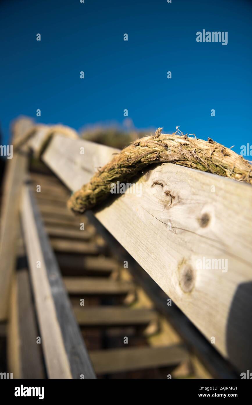 Close Up image of the hand rail of a coastal staircase linking property to Downderry Beach constructed of timber and thick twine Stock Photo