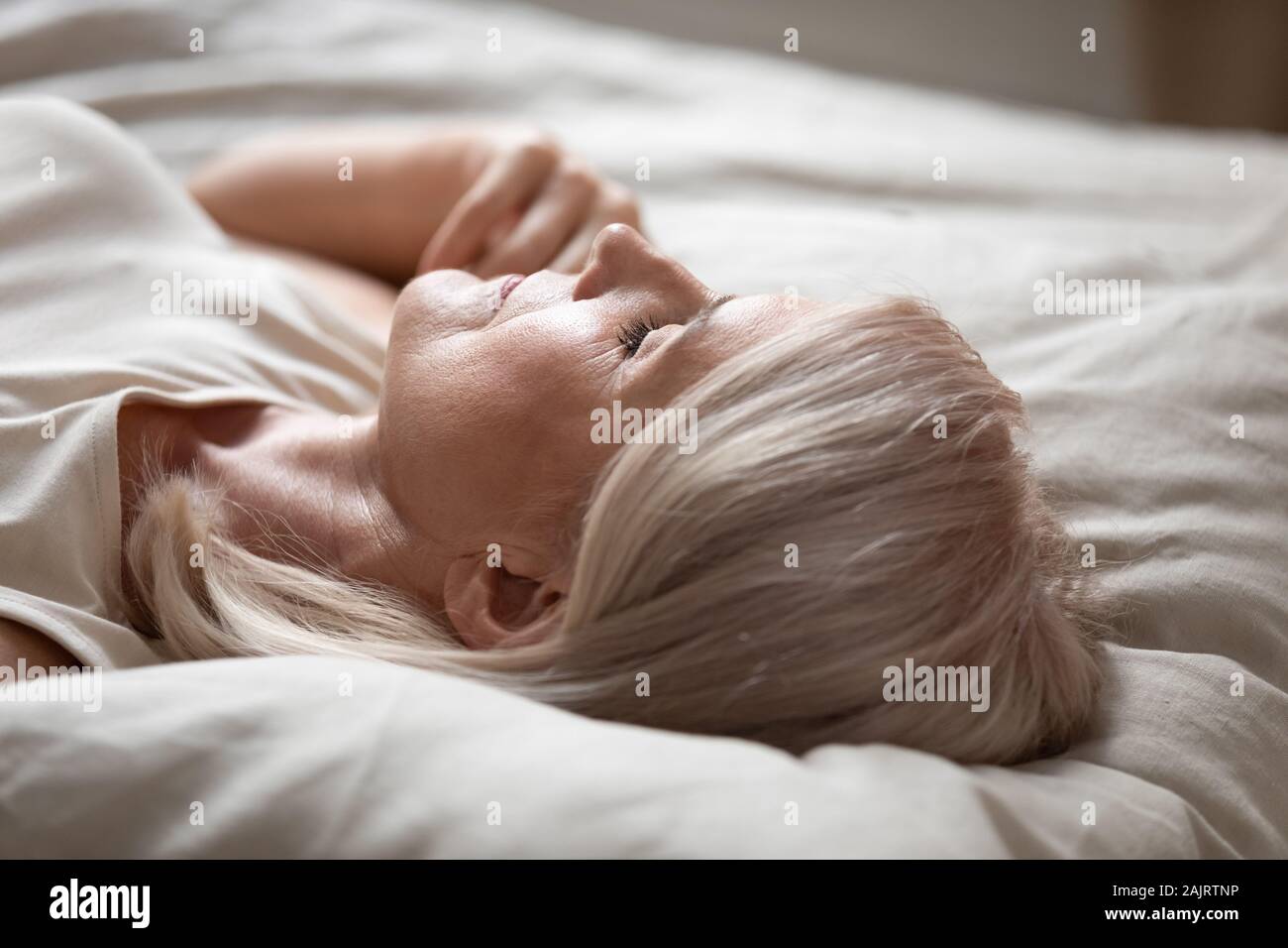 Tired mature woman relax sleeping in comfy bed Stock Photo