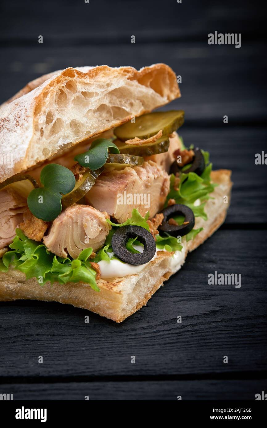 American fast food. Juicy tuna sandwich with cheese, salad and olives on a dark background. Club food Stock Photo
