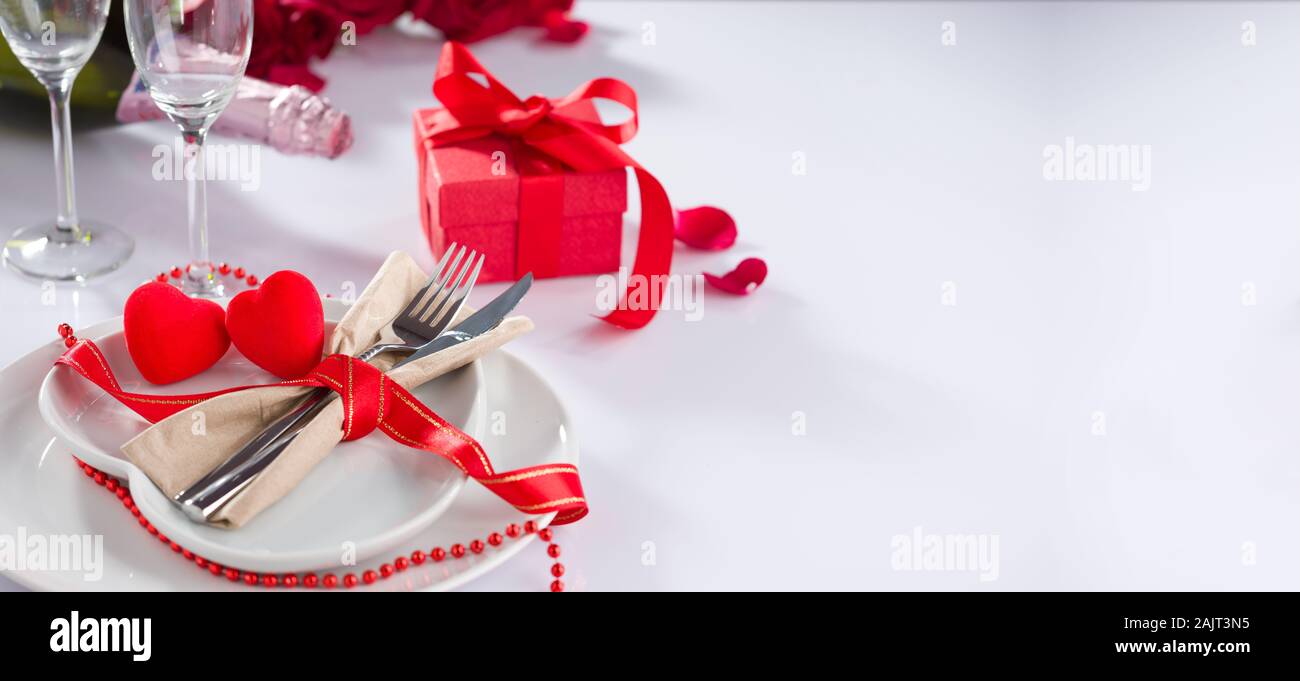 Valentine's day background. Fork and knife in heart plate on table. Champagne bottle, glasses and gift box on table Stock Photo