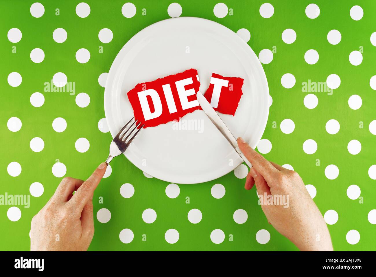 Female hands at dinner table holding fork and a knife above plate as dieting concept. Word Diet becoming Die reffering to health issues that diet mist Stock Photo