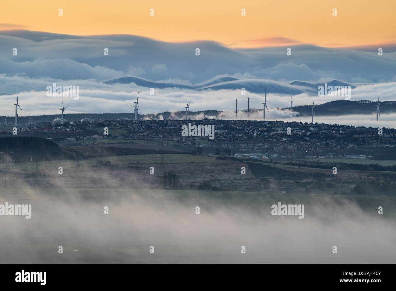 Wind farm, petrochemical plant and small town with Pentland Hills and rolling mist in the background. Stock Photo