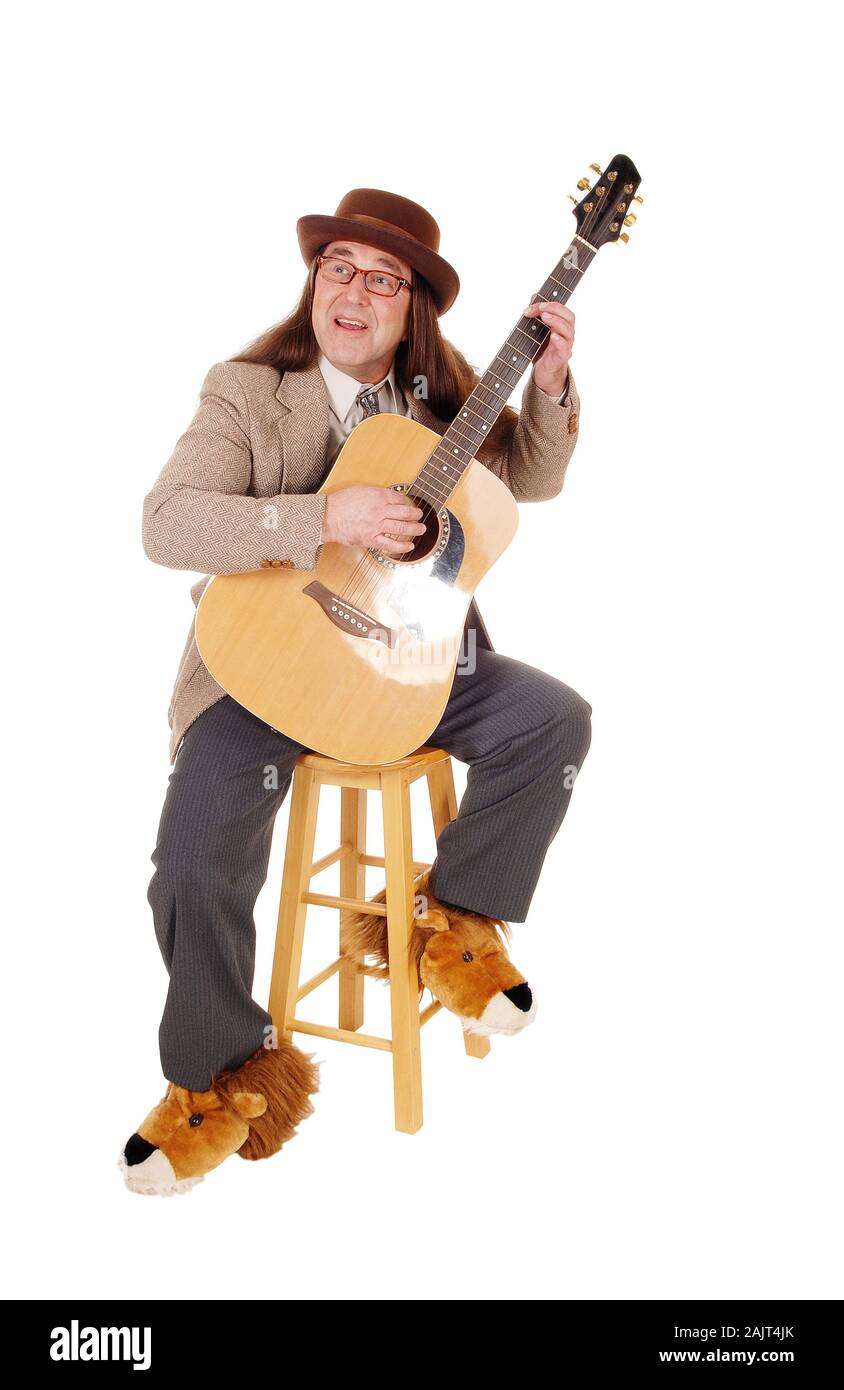 A middle age indigenous man in fancy shoes sitting and playing his guitar in a jacket and hat, isolated for white background Stock Photo