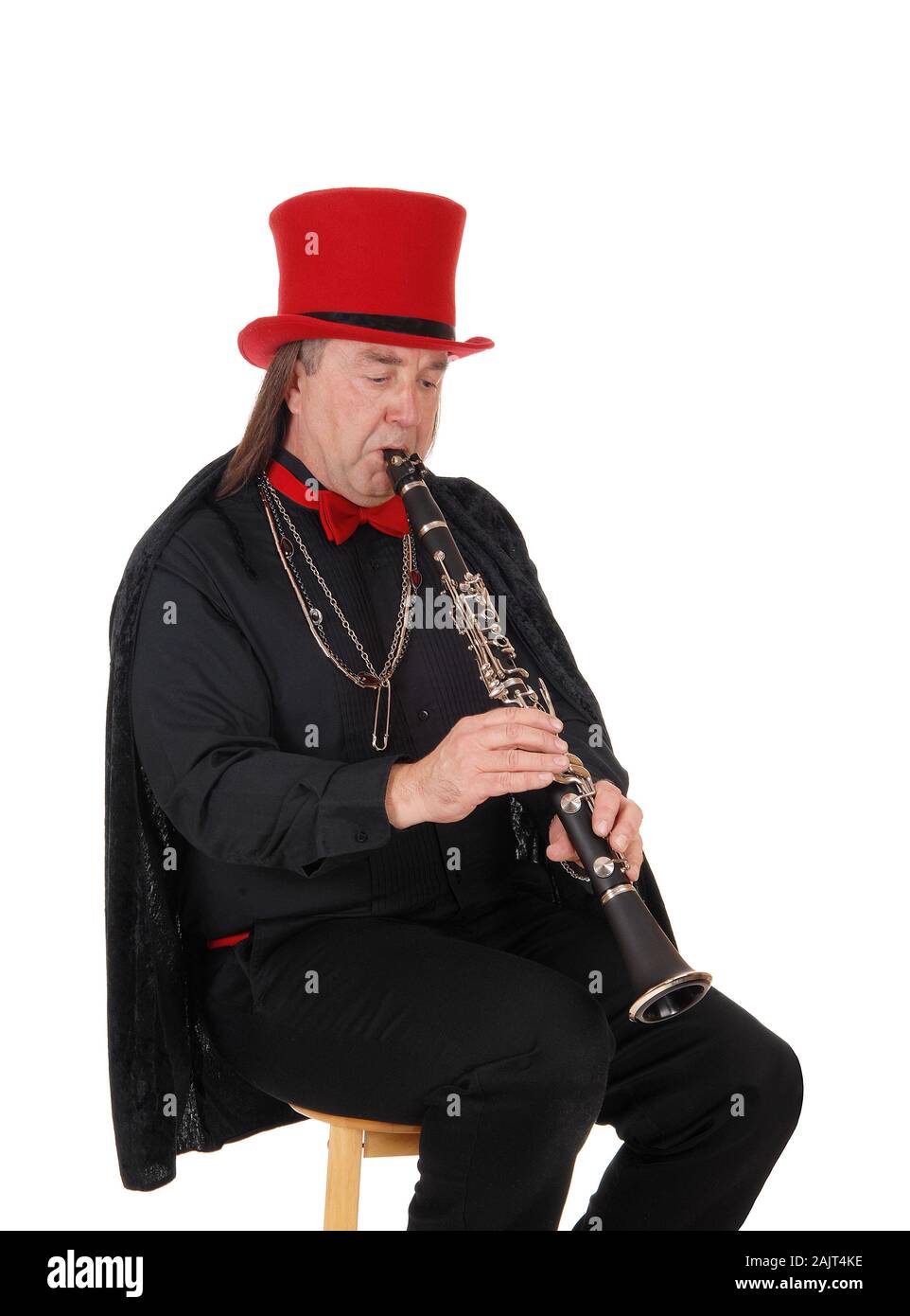 A middle age indigenous man playing his clarinet in a black outfit and red hat and bow, isolated for white background Stock Photo