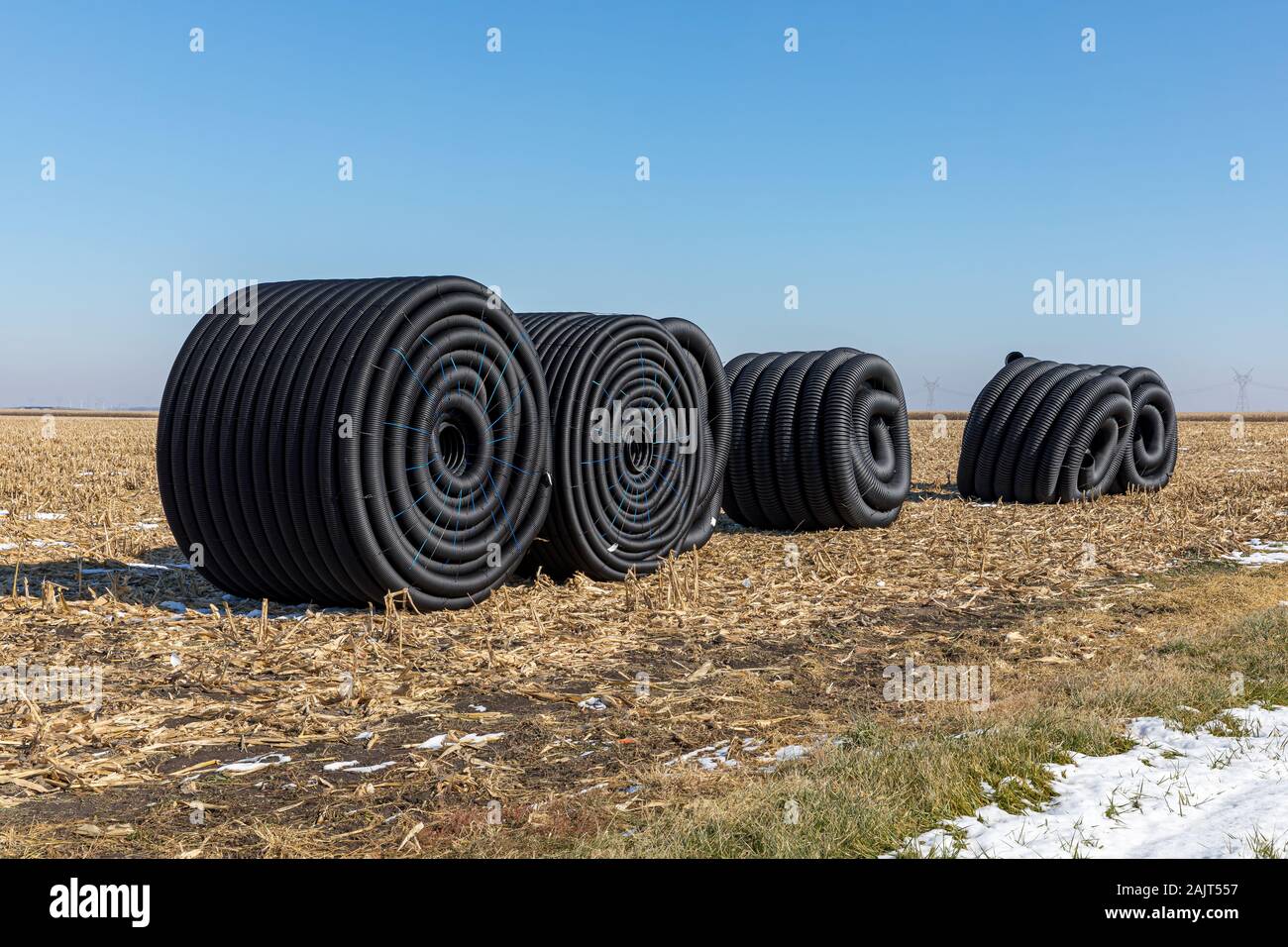 Coiled rolls of black perforated plastic drainage pipe, field tile, sitting in field after harvest ready to be buried underground during winter Stock Photo