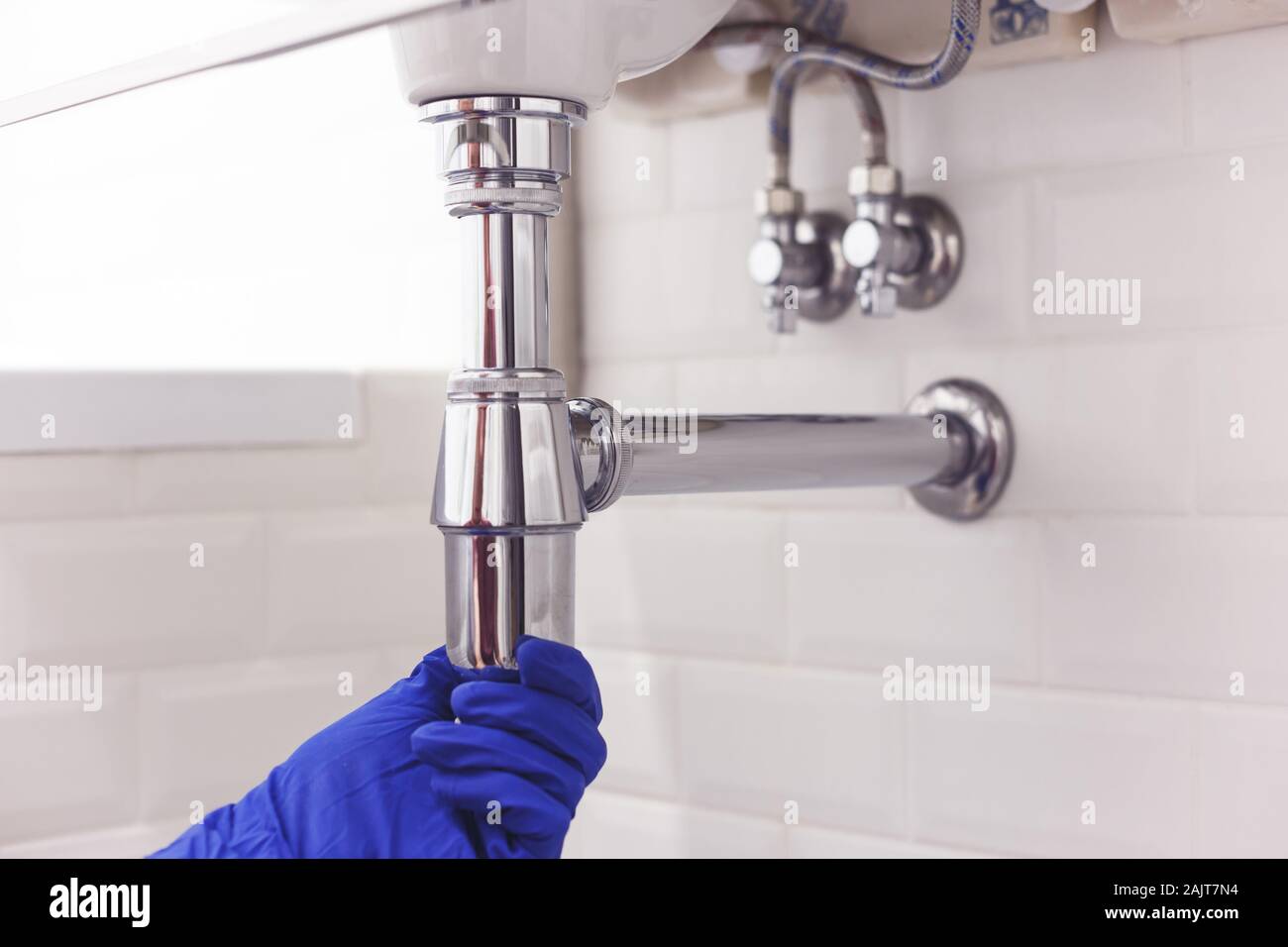 Plumber repairs and maintains chrome siphon under the washbasin