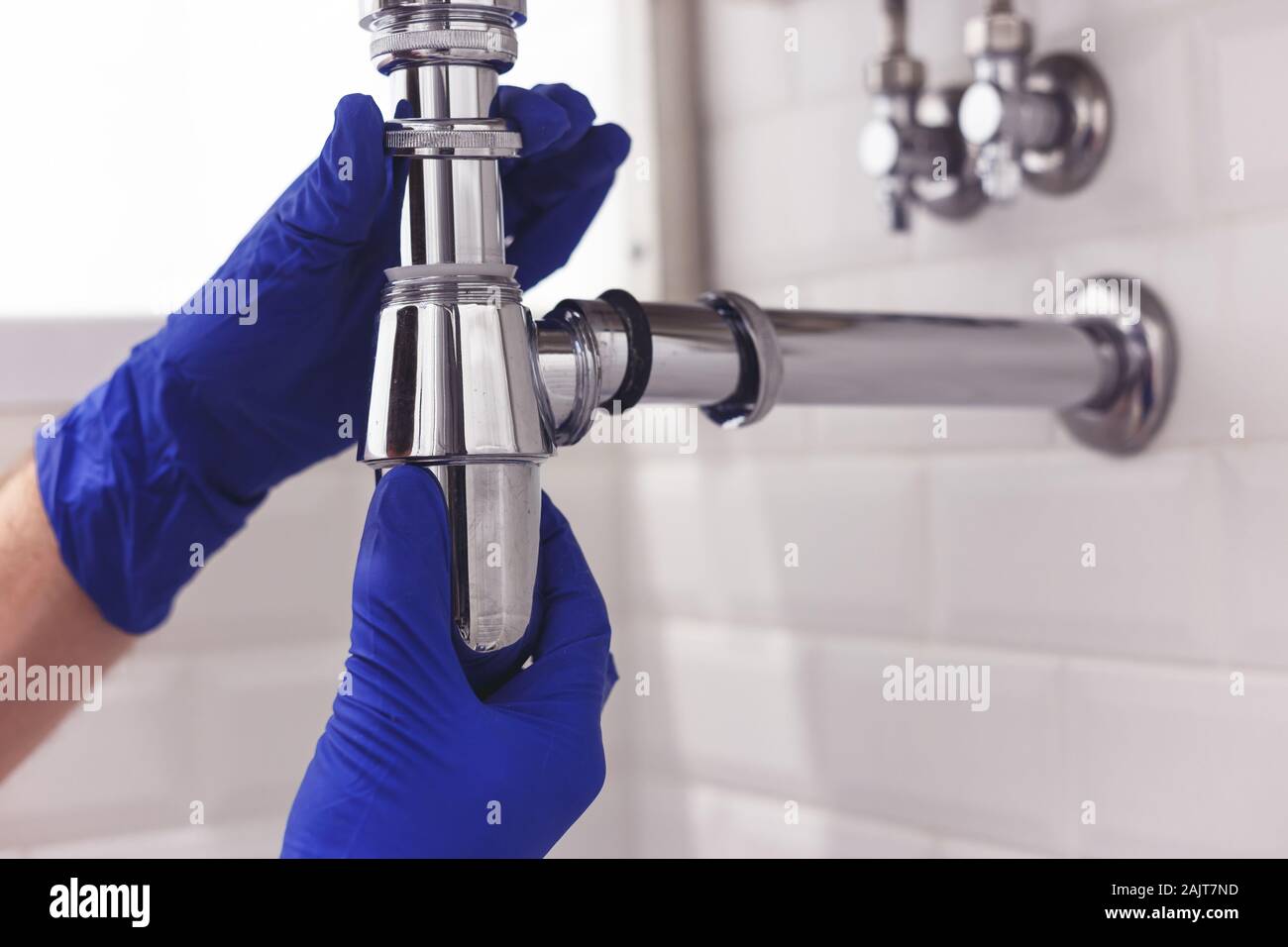 Plumber repairs and maintains chrome siphon under the washbasin