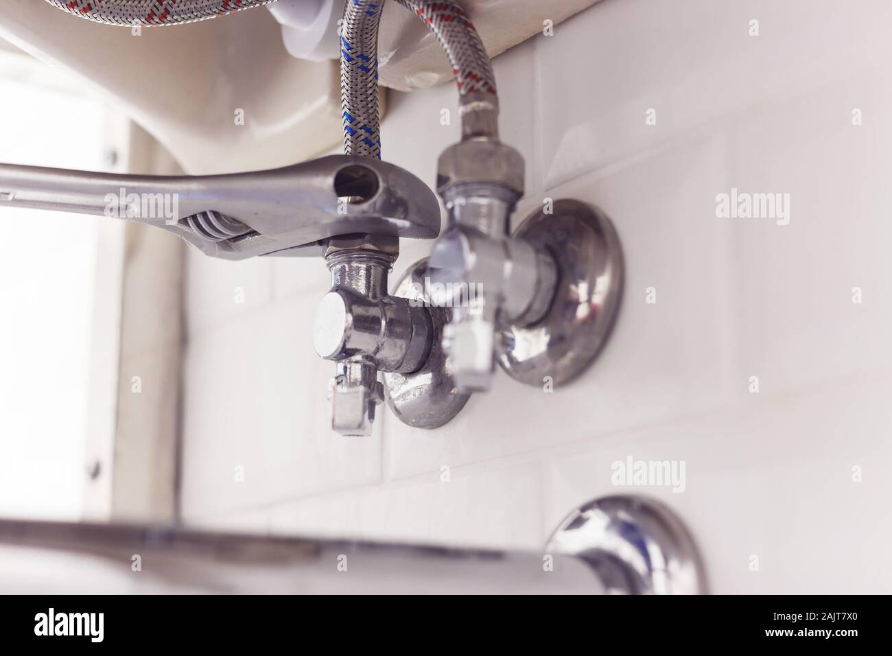 Plumber turns nut on angle valve under wash basin using spreading wrench. Stock Photo