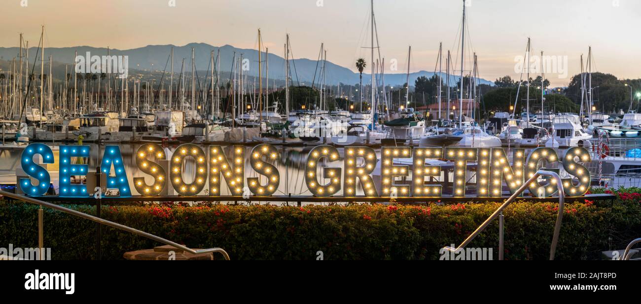 Seasons Greetings sign decorate the Ventura Harbor with the boats and masts in the background at dawn during the Christmas holiday. Stock Photo