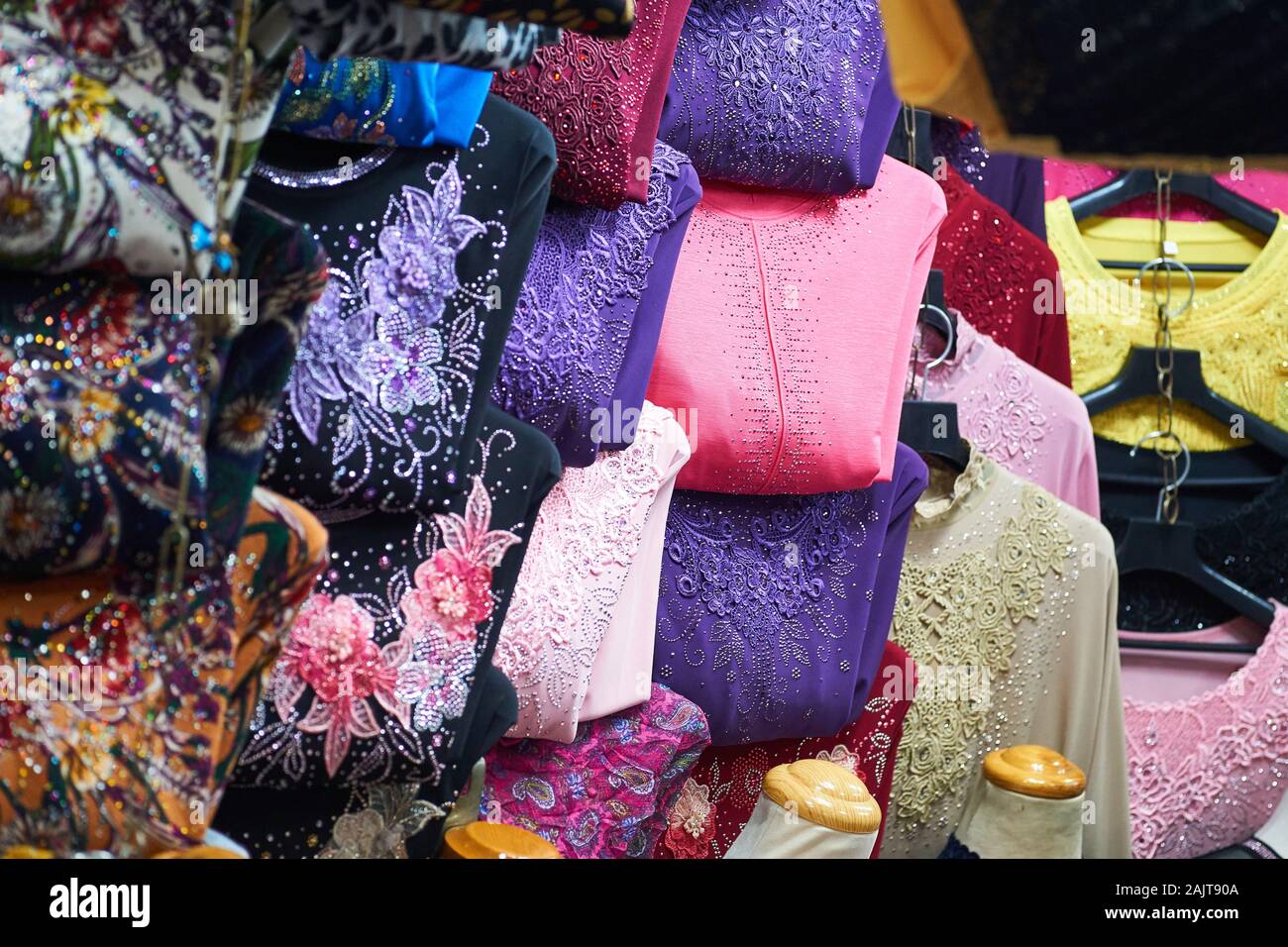 Vibrant and colourful shirts with beaded designs for sale on hangers at a clothing shop in