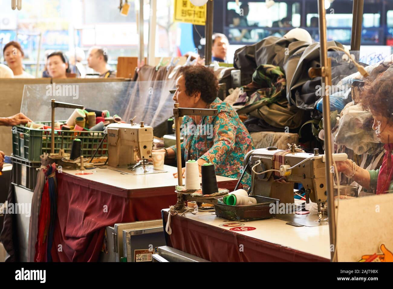 Seamstresses at Gwangjang Market performing clothing repairs with antique sewing machines at desks. Stock Photo