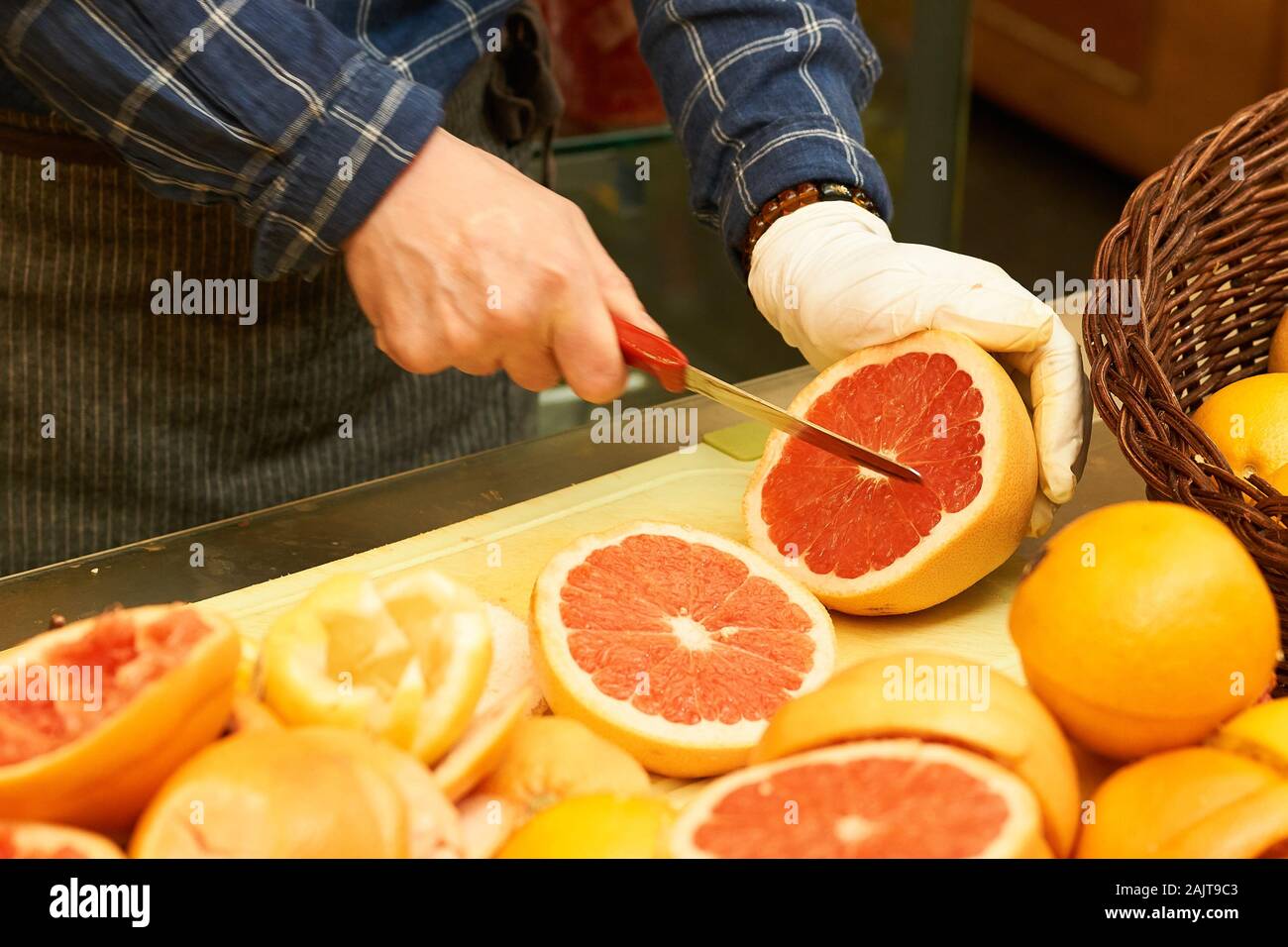A chef cuts pink fleshed grapefruits (Citrus × paradisi) in half for use in smoothies at a food stall in Gwangjang Market in Seoul, South Korea. Stock Photo