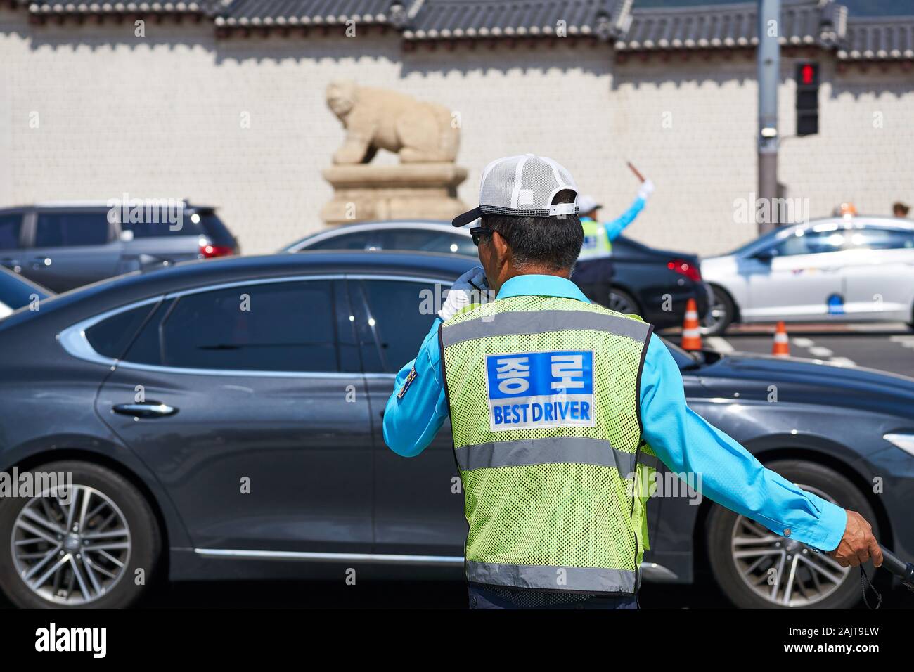 An official in a neon green vest with 'best driver' printed on it directs traffic in Seoul, in front of the Gwanghwamun Gate. Stock Photo