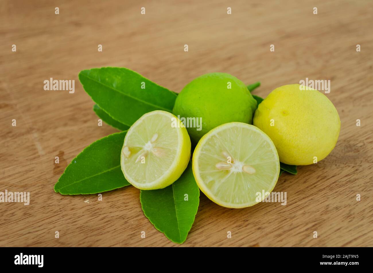 Whole And Cut Key Lime And Leaves On A Board Table Stock Photo