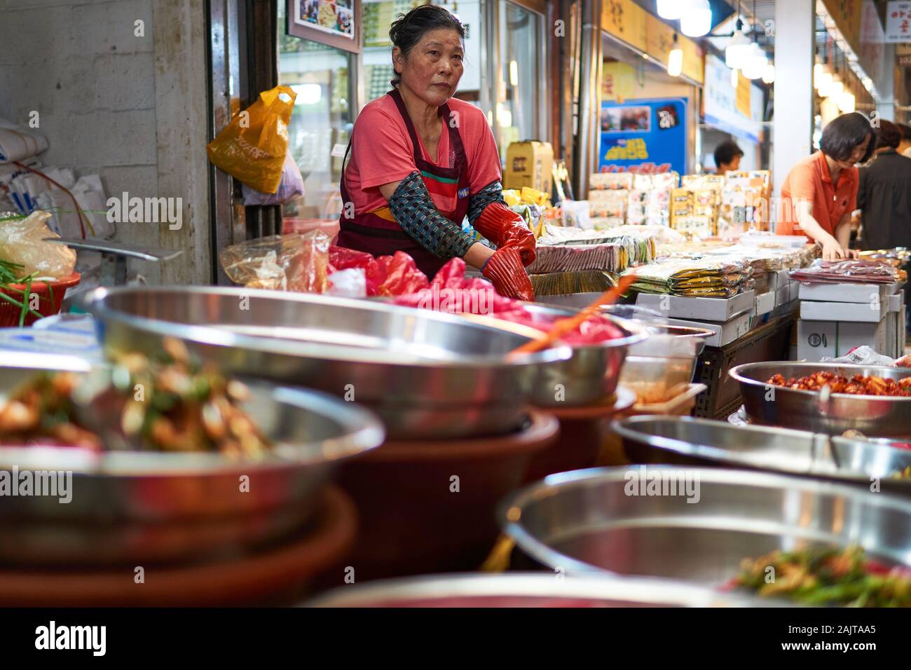 Mature, Korean woman puts on rubber gloves to serve Kimchi at Gwangjang Market in Seoul, South Korea. Stock Photo