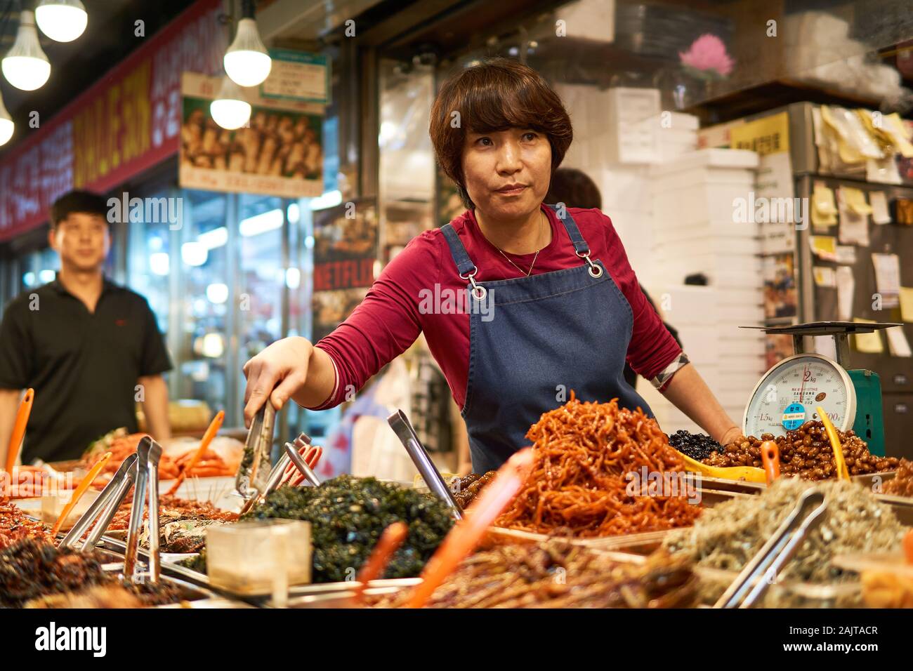 Female chef serves food with tongs at Gwangjang Market in Seoul, South Korea. Stock Photo
