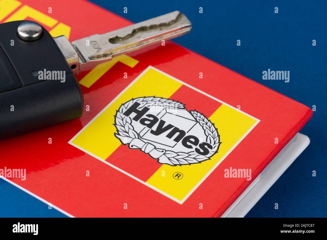 A Haynes manual pictured with a set of car keys on a blue background. Stock Photo
