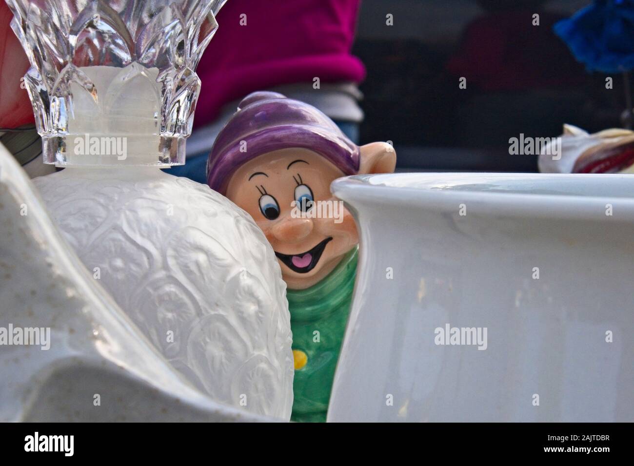 Disney's seven dwarfs dopey figurine peering through antique glassware at a flea market Stock Photo