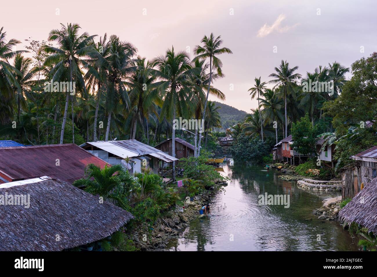 Woman washes clothing in small village along river at sunrise Stock Photo