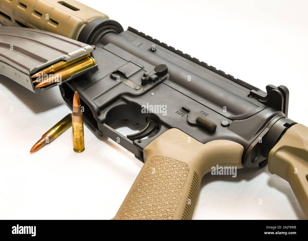 A multi colored AR15 rifle with a rifle magazine loaded with 223 caliber bullets on it with 2 of the same bullets in front of it on a white background Stock Photo