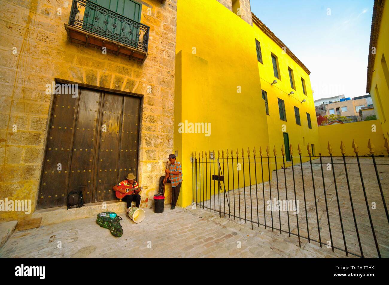 Two musicians perform beside a yellow wall in Havana, Cuba Stock Photo