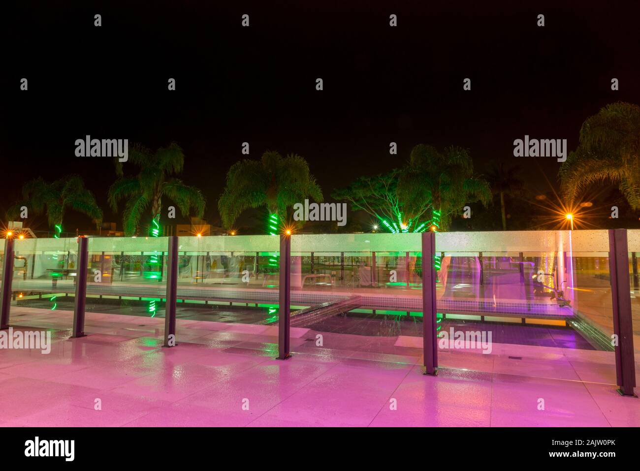 Long exposure of a palm-fringed pool area in the background with spiraling green lights on its logs. Stock Photo