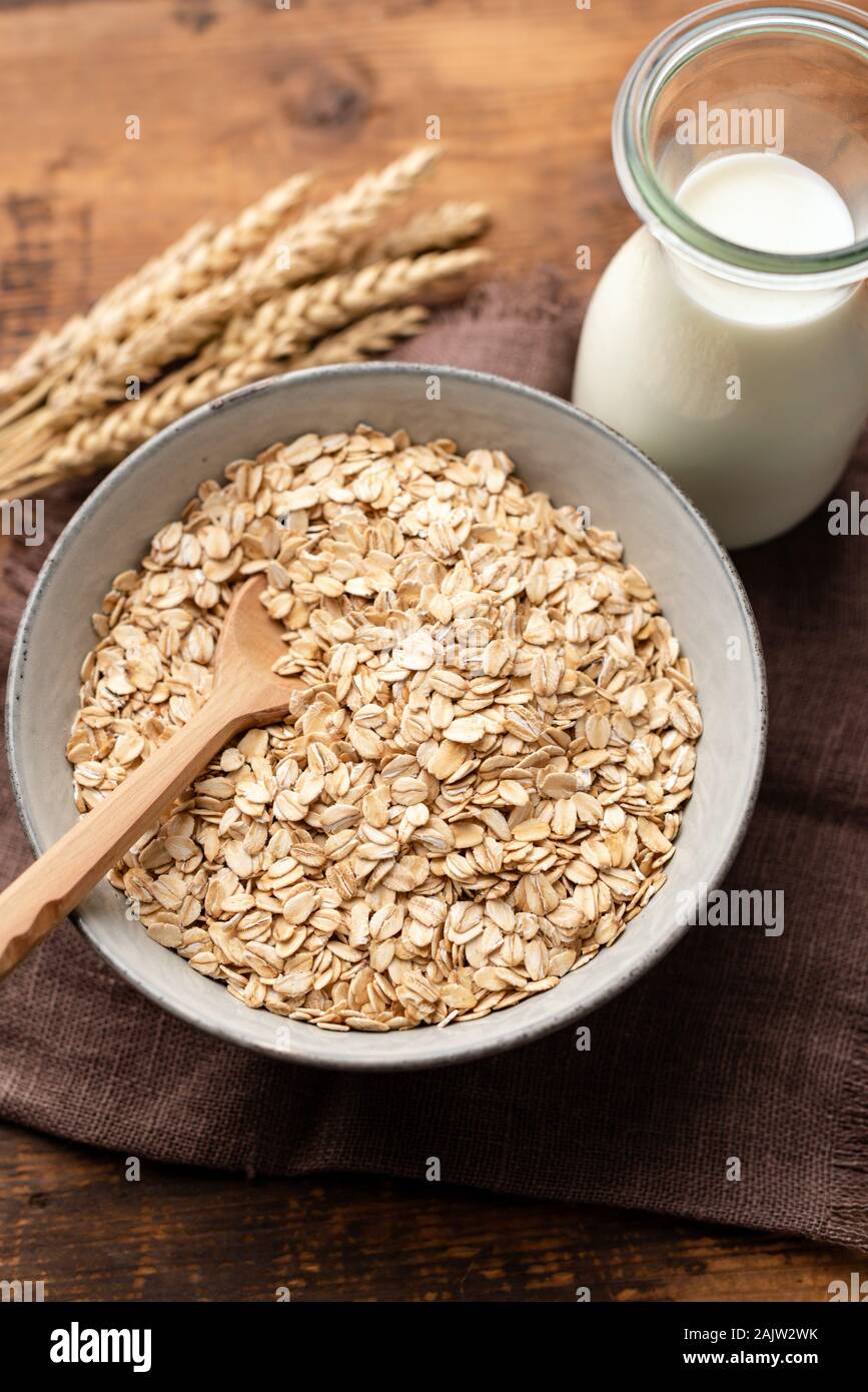 Oatmeal, oat flakes, rolled oats and vegan oat milk in bottle on a wooden table. Healthy breakfast food, clean eating, dieting concept Stock Photo