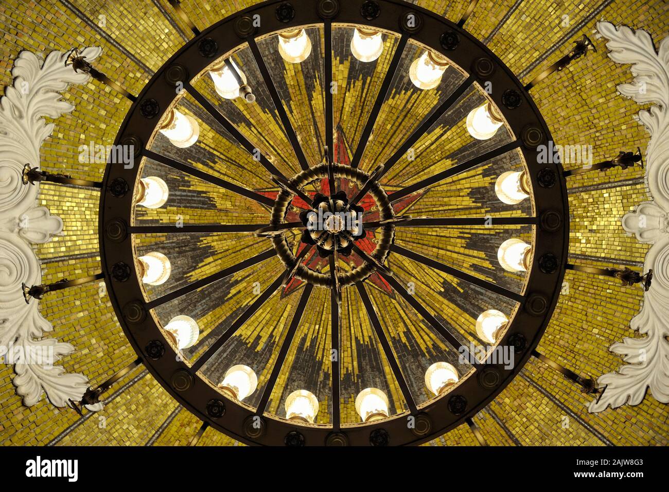 = Under Chandelier and Mosaic Panel of Red Star with Gold Beams =  Directly below view of illuminated bronze chandelier hanging from a dome in interme Stock Photo