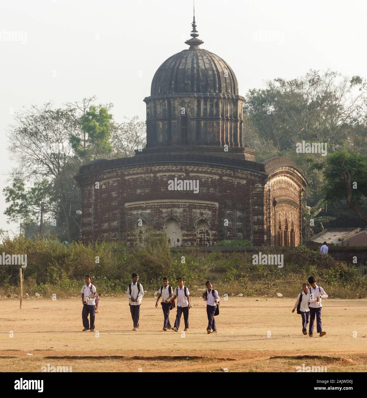 Bishnupur, West Bengal, India - February 6, 2018:  Kids walk back from school, the ancient Radha Shyam temple in the background. Stock Photo