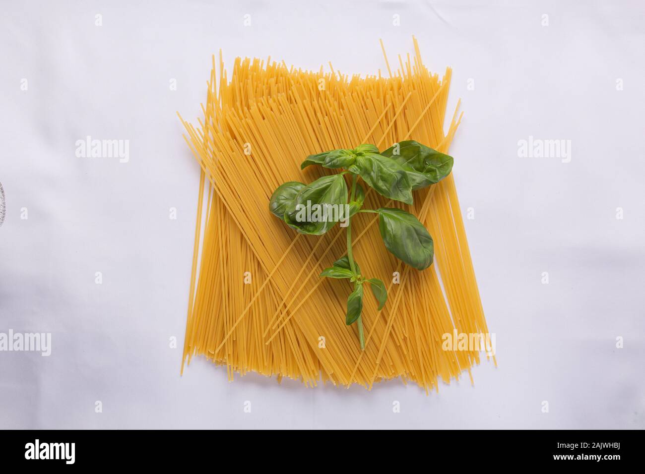 Pile of uncooked spaghetti and basil leaves on a white tablecloth Stock