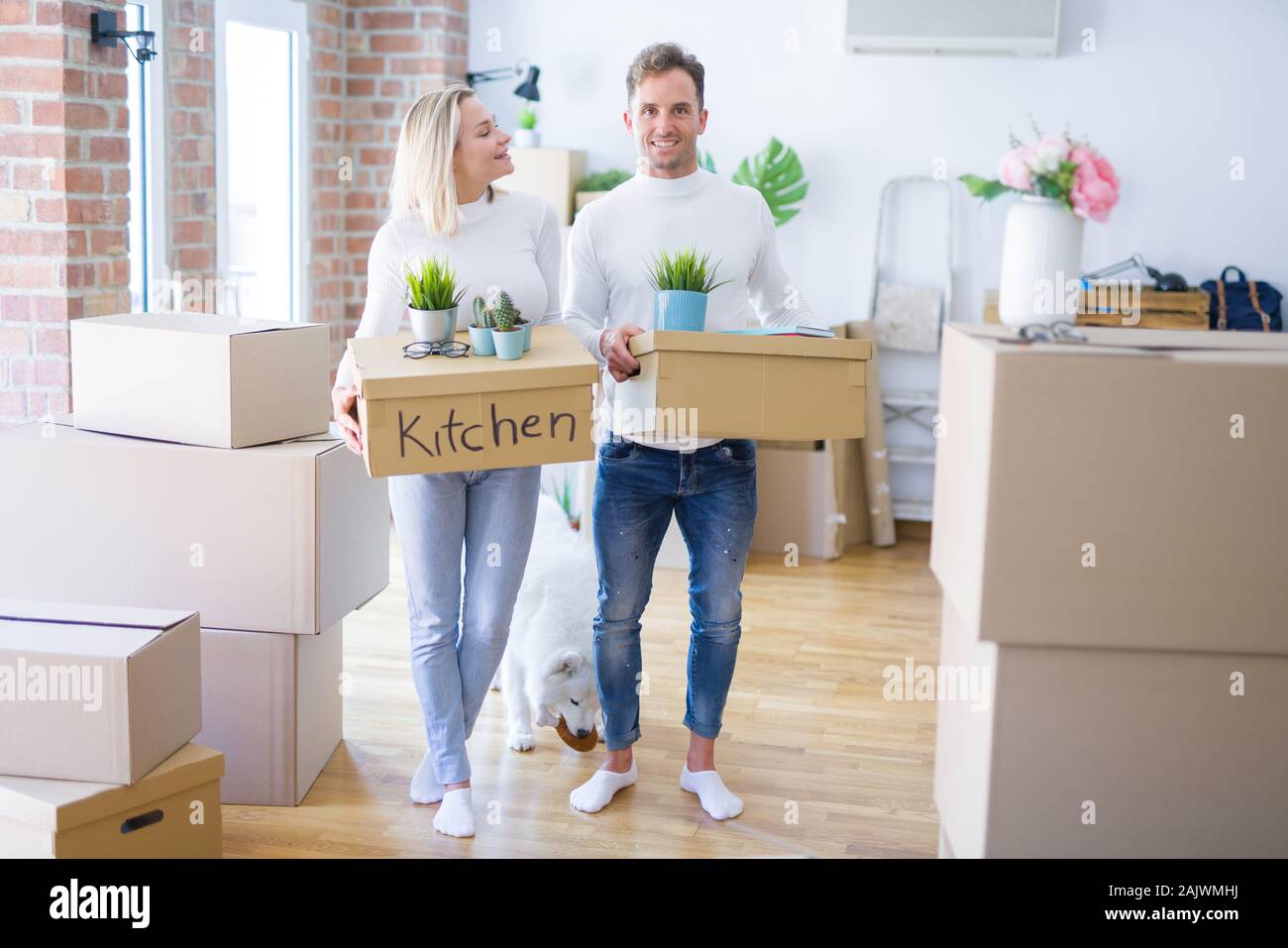Young beautiful couple with dog moving cardboard boxes at new home