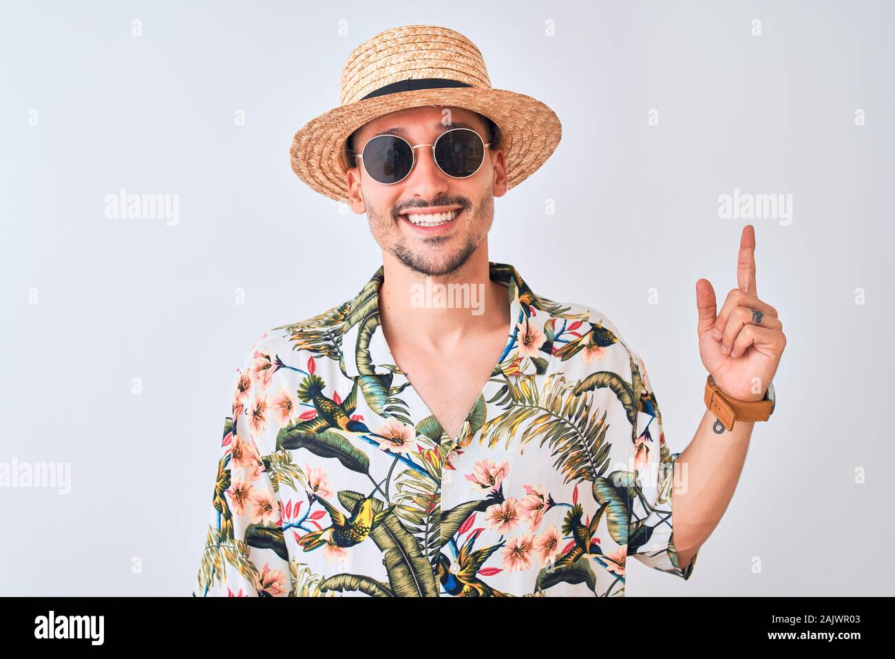 Young handsome man wearing Hawaiian shirt and summer hat over isolated ...