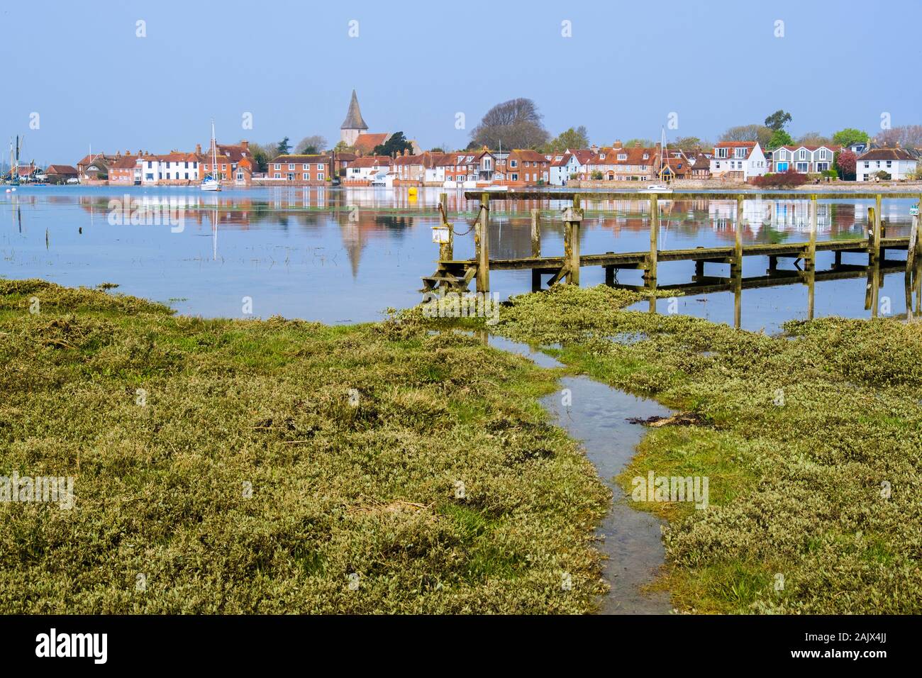 View across salt marsh to old village reflected in still waters of Bosham Creek at high tide in Chichester harbour. Bosham, West Sussex, England, UK Stock Photo