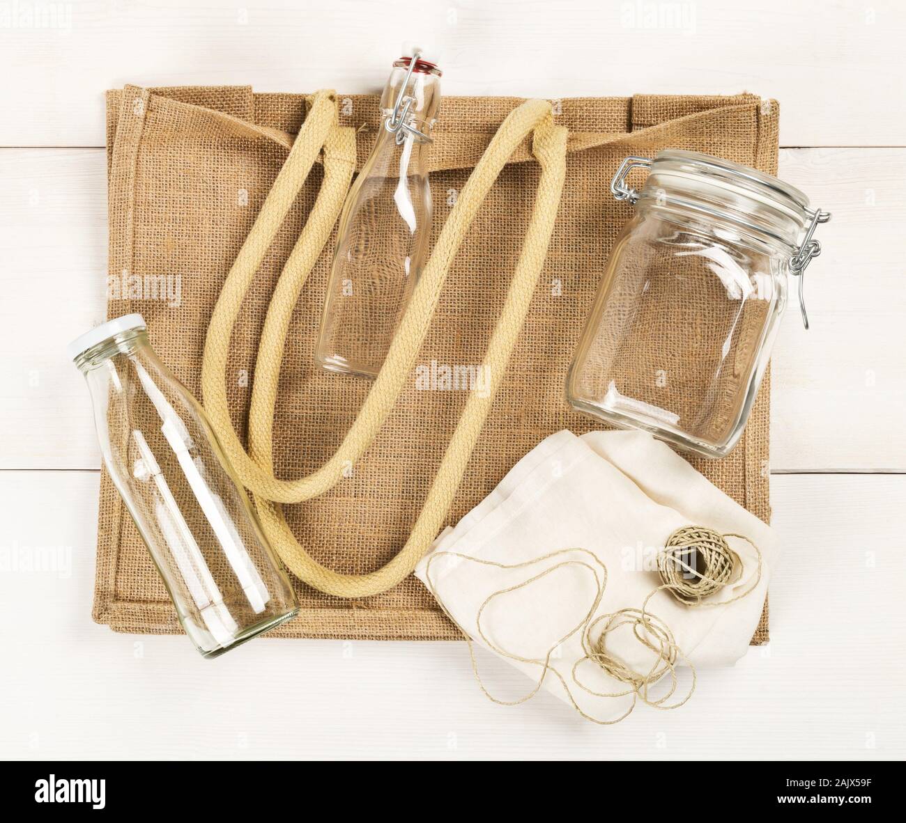 Zero waste or waste free shopping utensils with burlap bag, glass bottles and cotton bag on white wooden table background flat lay from above - waste Stock Photo