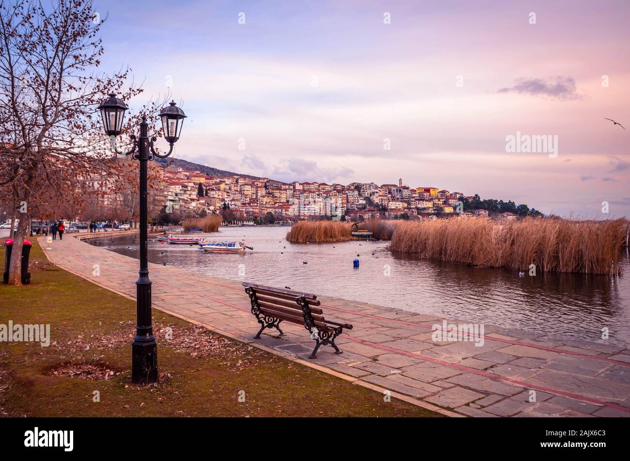Atmospheric view of city of Kastoria and Orestiada lake at sunset.The promanade with bench and street lights in foreground. Stock Photo