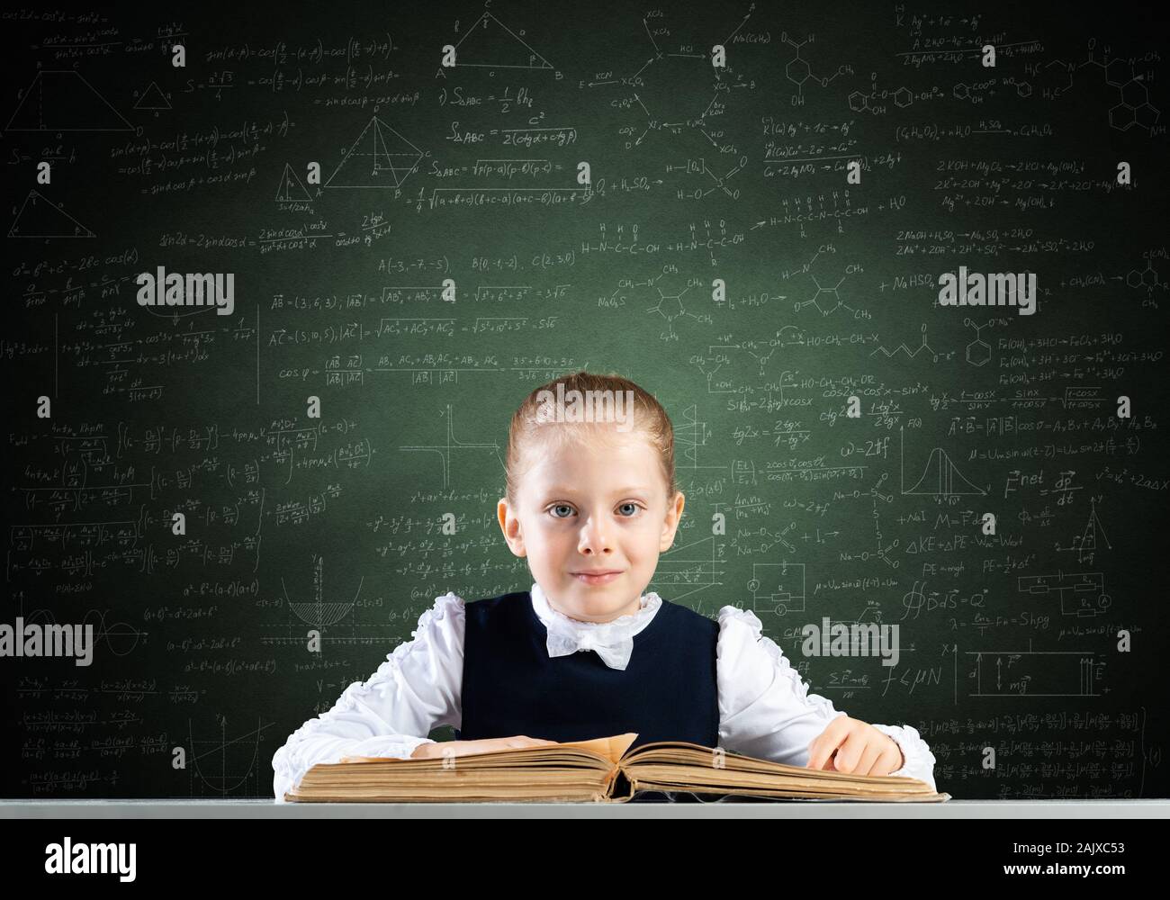 Smiling little girl sitting at desk with open book Stock Photo - Alamy