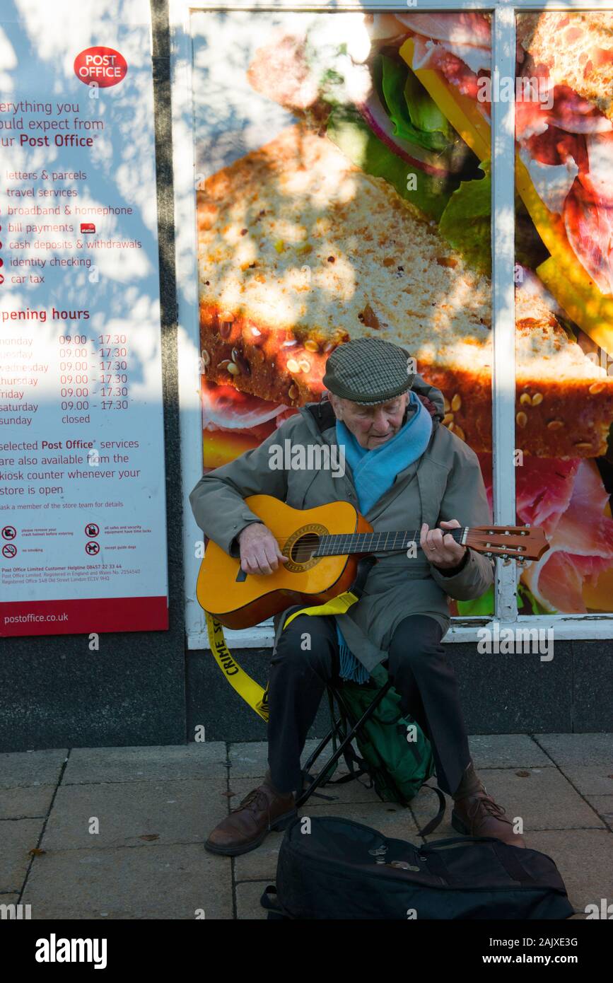 Old man with guitar busking outside the Co-op and post Office on Spring Gardens, Buxton, England Stock Photo