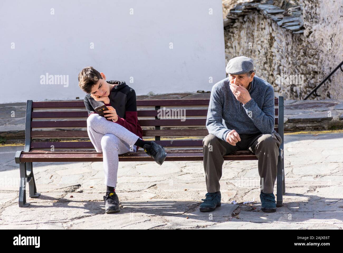 Capileira, La Alpujarra, Alpujarras, Granada region, Andalusia, Spain. A youth plays on his mobile phone sitting next to a senior man in the village s Stock Photo