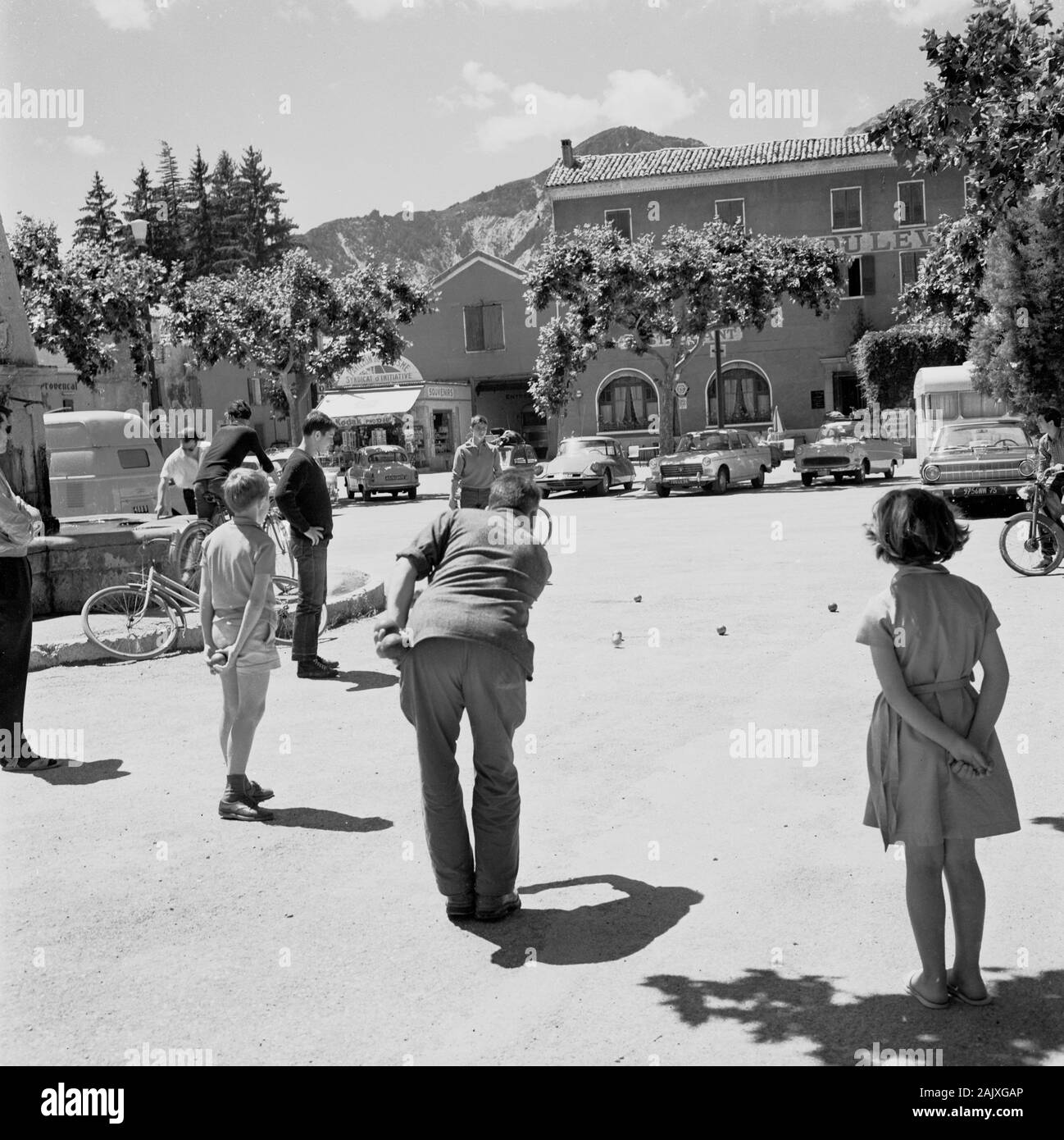1950s, historical, Cotes de sur, France, summertime and a man and children in a village square playing boules, a traditional french game playe with metallic balls on a dirt surface. A popular game, similar to bowls, it is also known as petanque. Stock Photo