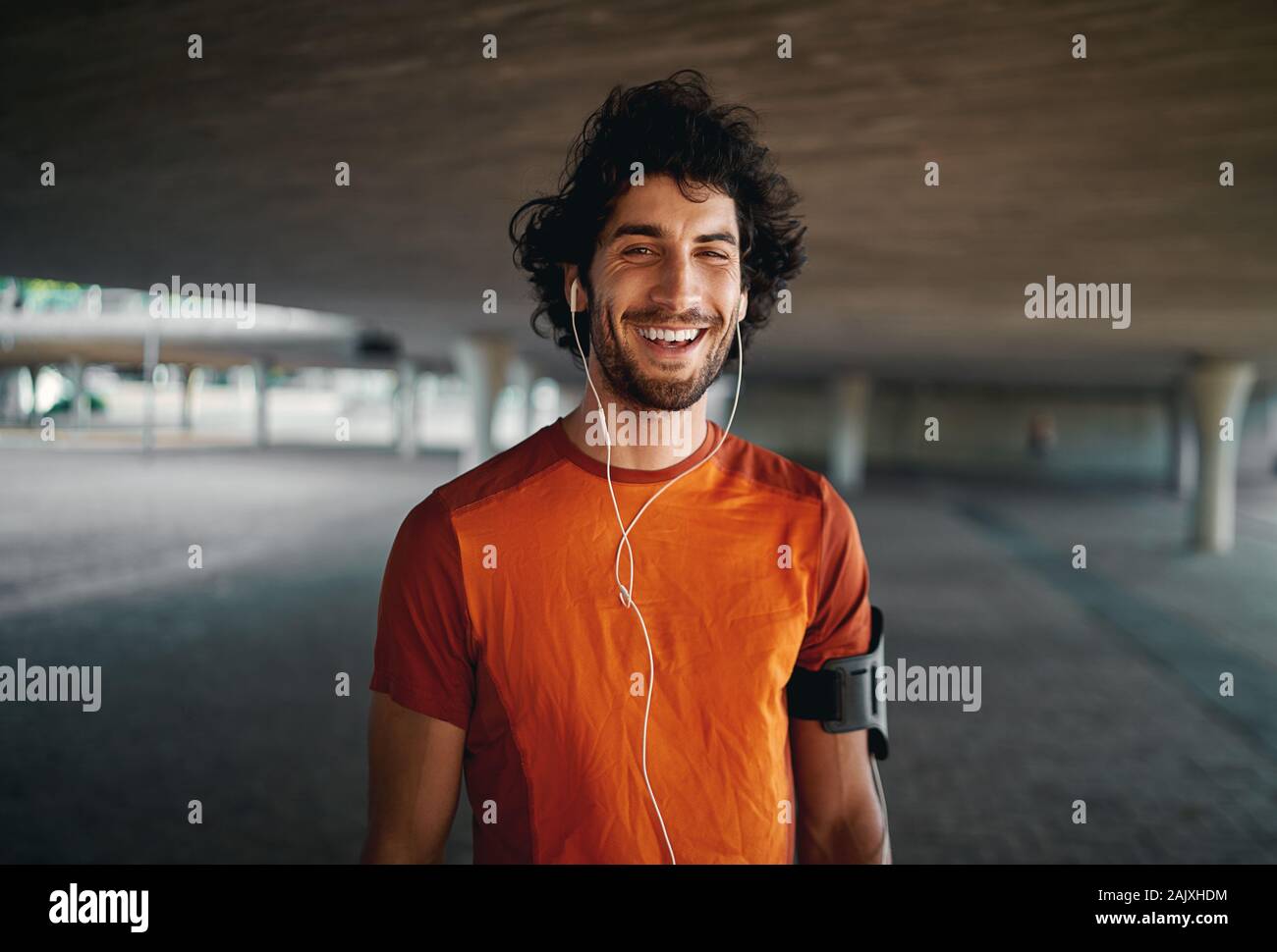 Cheerful portrait of a healthy sporty young man enjoying listening to music on earphones standing on city street Stock Photo