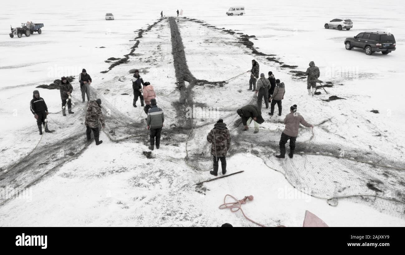 Chinese workers pull a giant fishing net to expect a good harvest on the frozen Wolong Lake in Kangping County, Shenyang City, northeast China's Liaon Stock Photo