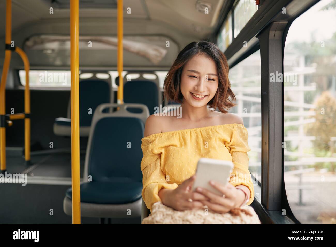 young beautiful asian woman browsing and typing messages in a public bus Stock Photo
