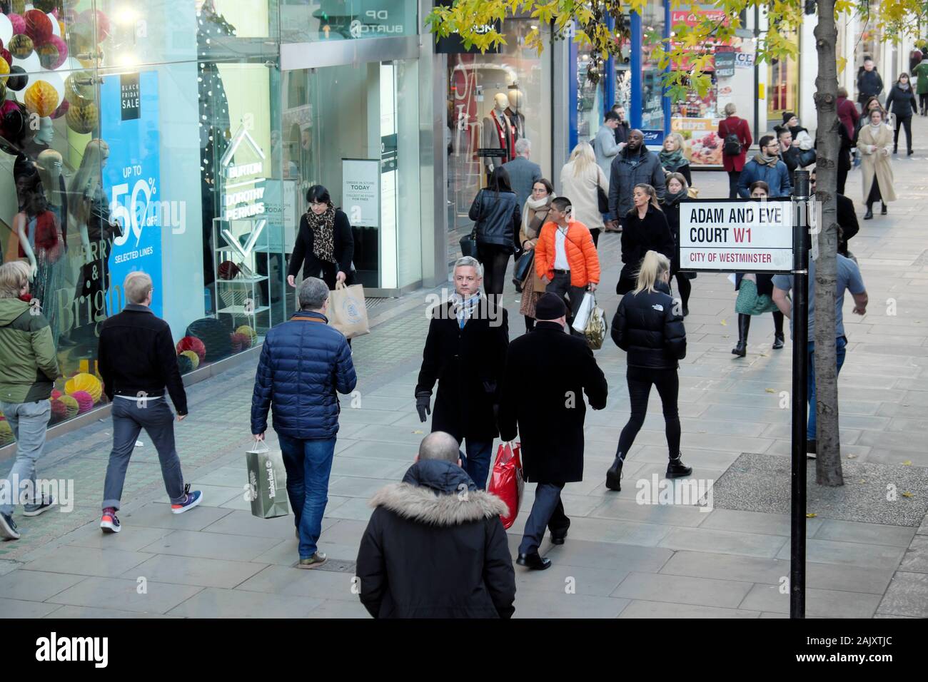 Shoppers at Christmas walking past Adam and Eve Court W1 street sign on