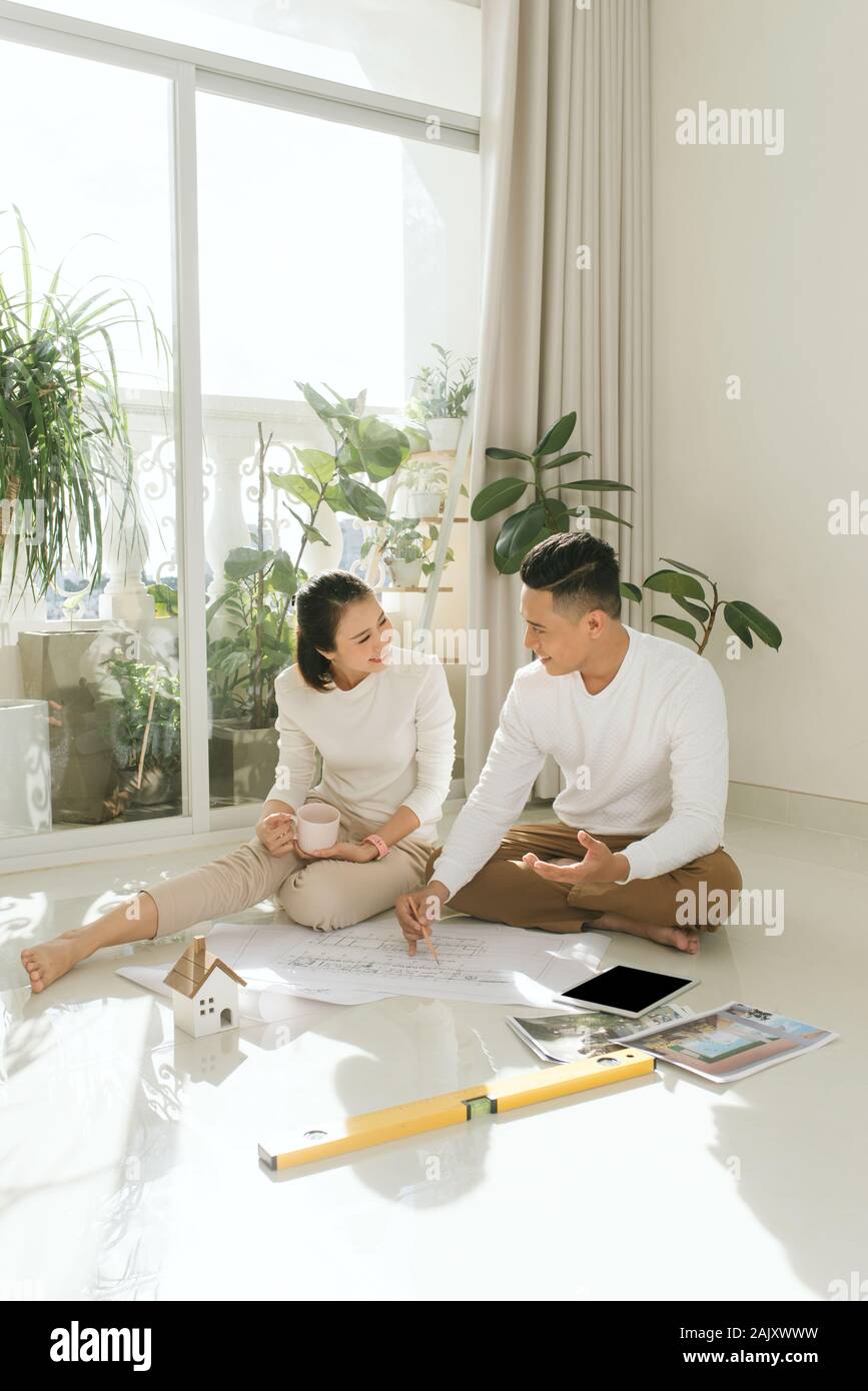 Young couple sitting at floor moving into new home looking at floor plans together Stock Photo