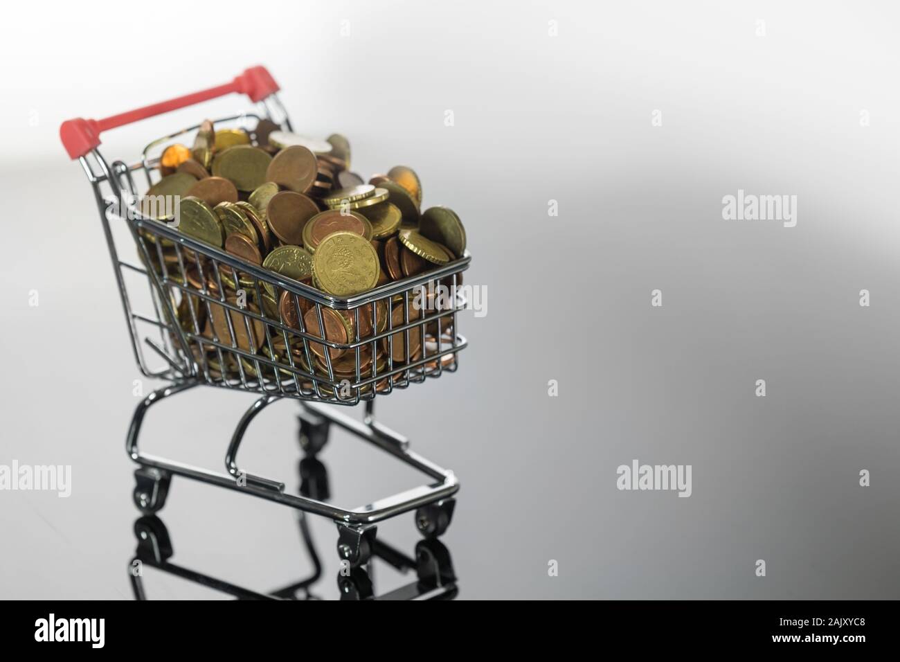 Three-Quarter Side View of Tiny Shopping Trolley Full of Euro Coins on Reflective Surface Stock Photo