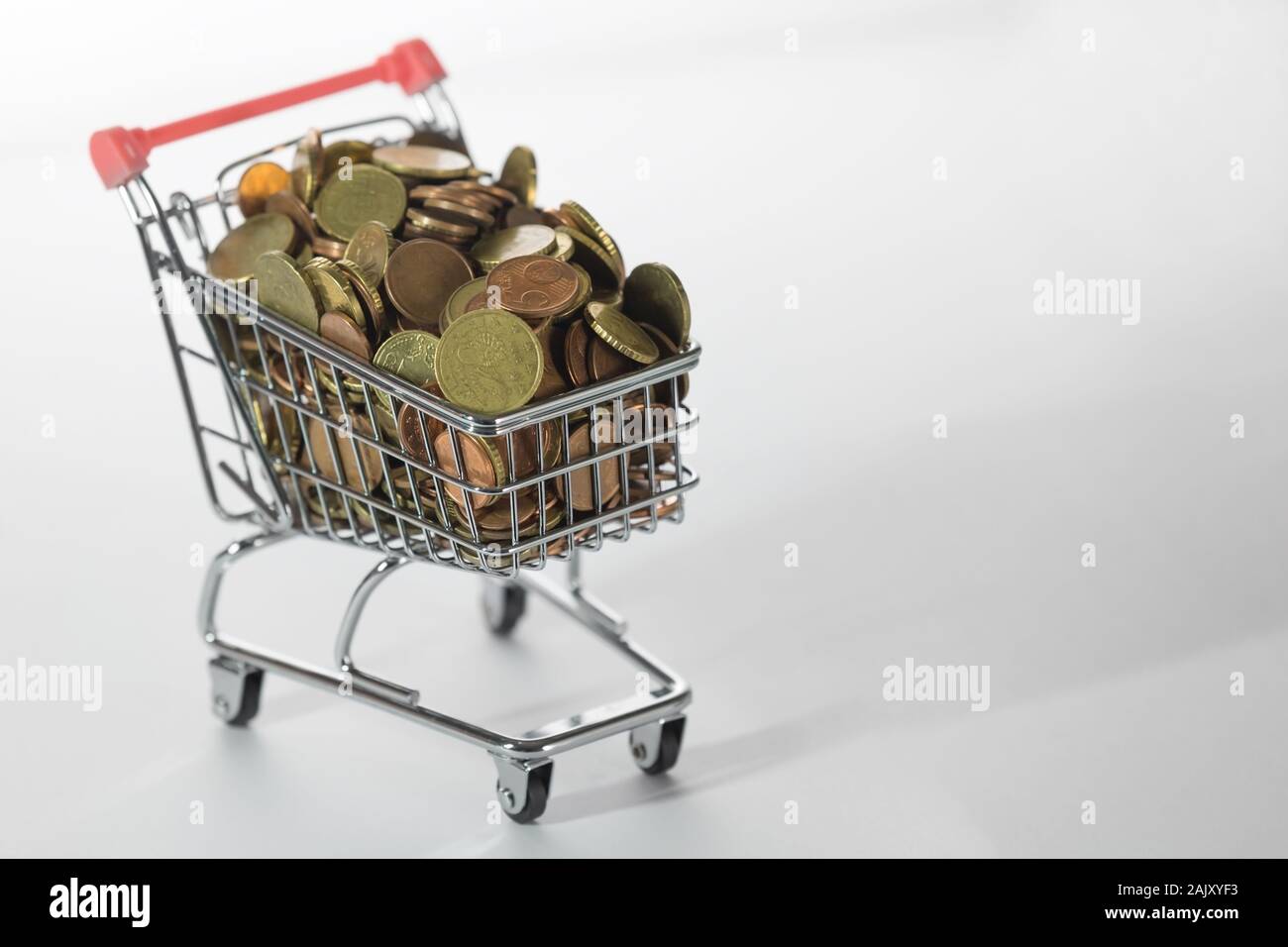 Three-Quarter Side View of Tiny Shopping Trolley Full of Euro Coins on White Stock Photo